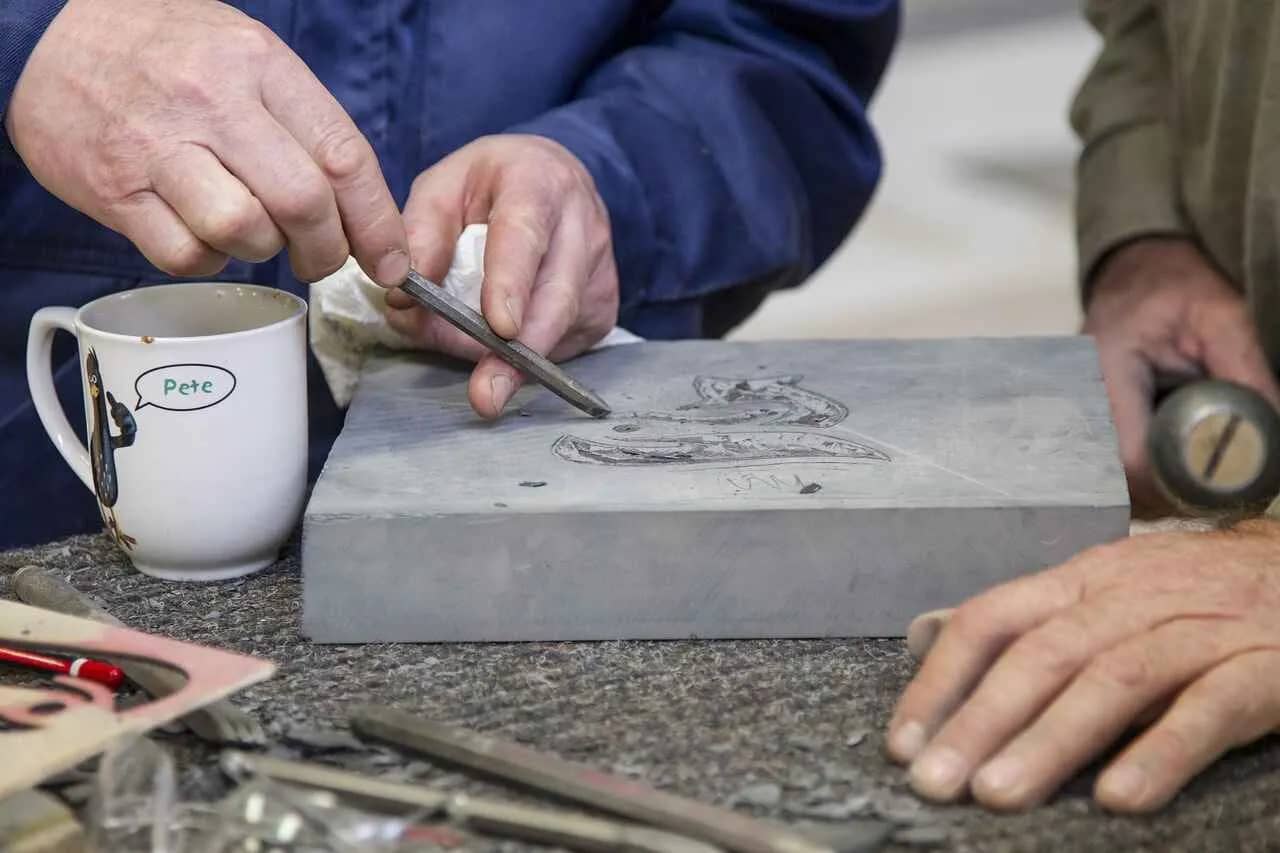 A woman is working on a piece of slate with a chisel which is a a Unique Hobby for Women