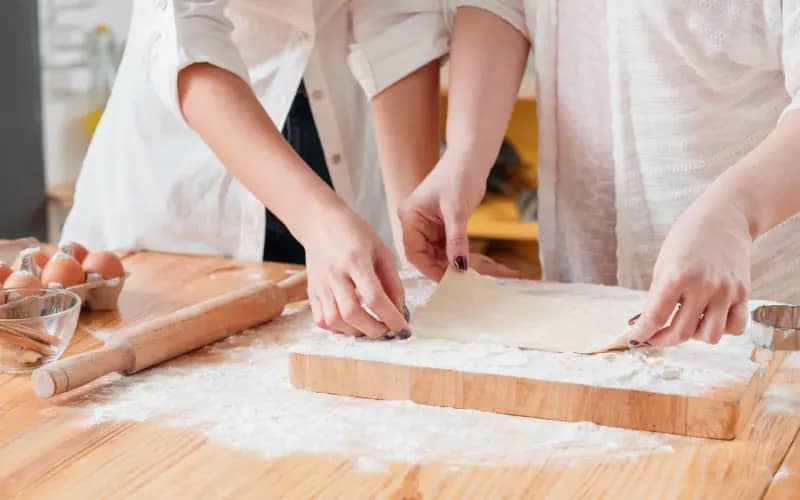 Two women in their 20s baking together at home, making dough as a relaxing indoor hobby.