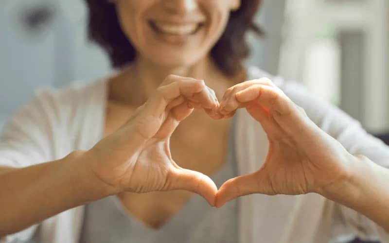 Woman in her 30s making a heart shape with her hands, symbolizing hobbies for women in their 30s near me and self-care activities.