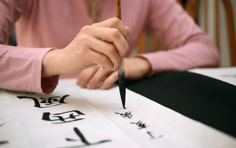 Woman in her 30s practicing calligraphy with a brush on paper, ideal indoor hobby for women in their 30s with kids or looking for creative activities.