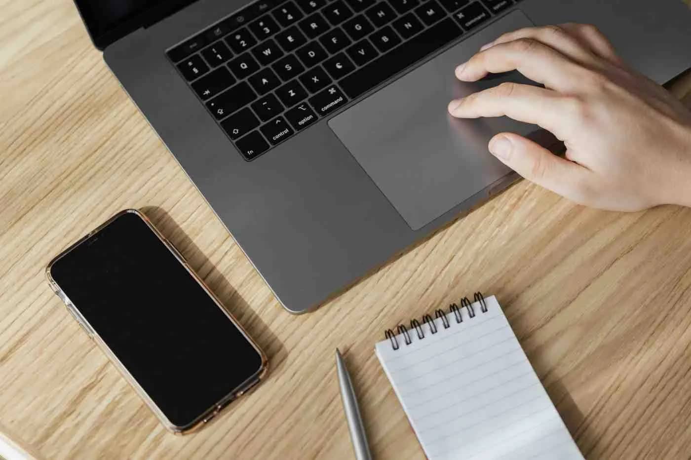 A laptop with a blank smartphone and notebook beside it, suggesting a person working or pursuing digital hobbies.